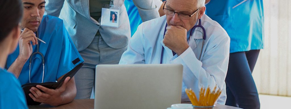 Profissionais da saúde analisam dados em frente a um laptop. Como é Feita a Auditoria em Saúde e Como Ela Ajuda na Gestão de Sinistro?