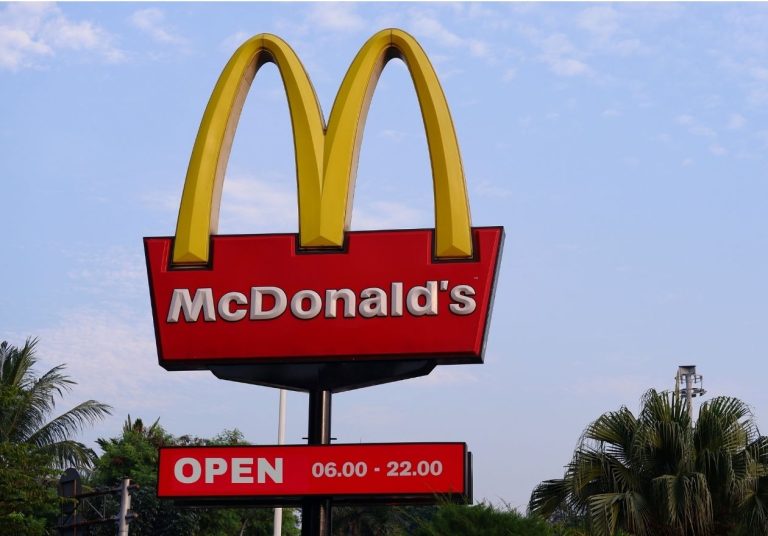 Um letreiro do McDonald's com os arcos dourados e horário de funcionamento ao ar livre. Curso: Aprenda com Ray Kroc.