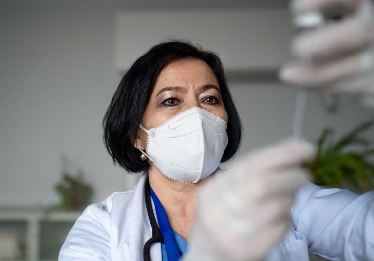 Profissional de saúde com máscara e luvas ajusta algum equipamento médico em ambiente hospitalar. Curso: Assistência Multi Covid-19.