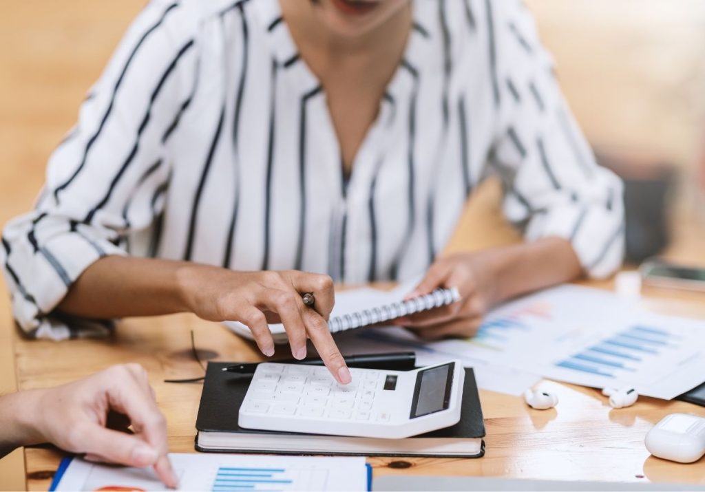 Uma mulher analisa gráficos e papéis financeiros em uma mesa com calculadora e caderno. Curso: Contabilidade para Não Contadores.