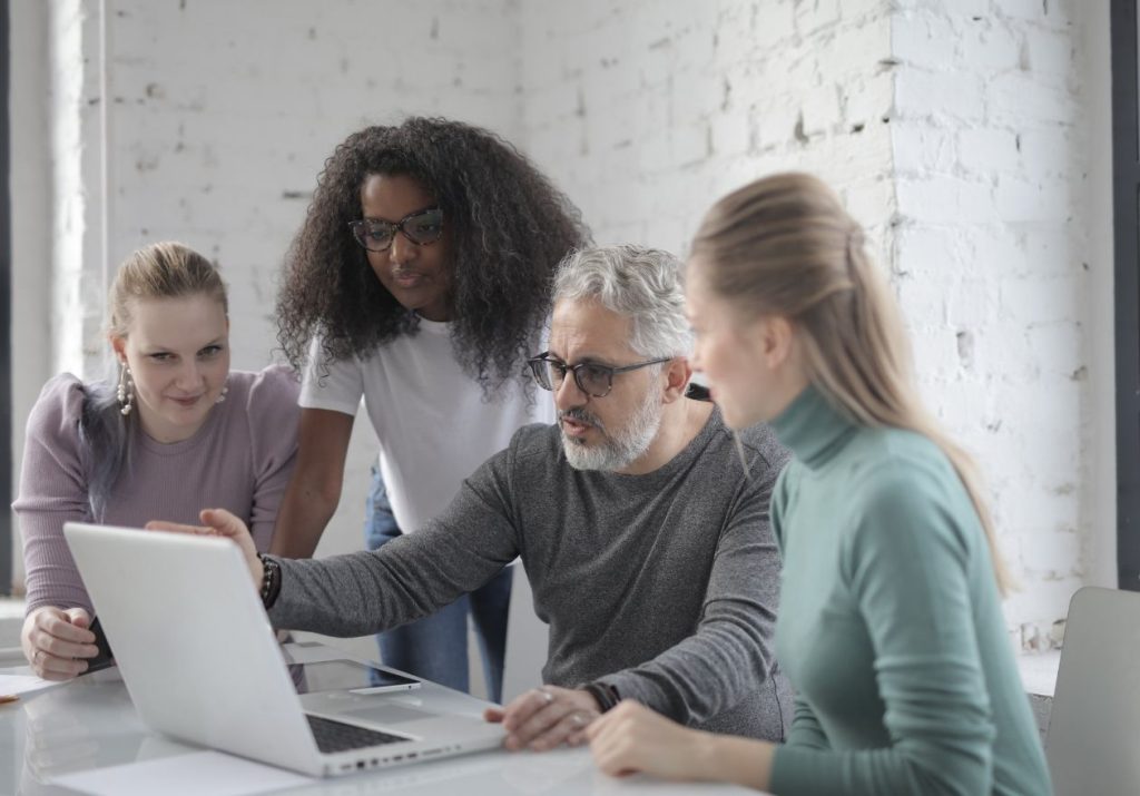 Equipe analisa dados em laptop, em sala com parede de tijolos. Curso: Gestão de Riscos em Operadoras de Planos de Saúde.