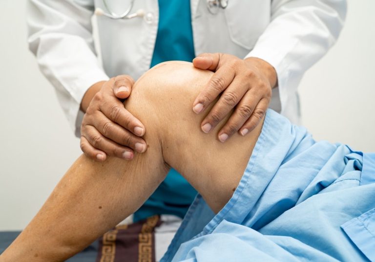 Médico examina o joelho de um paciente, manipulando a articulação em um ambiente hospitalar. Curso: Lesões do Ligamento Cruzado Anterior (LCA).