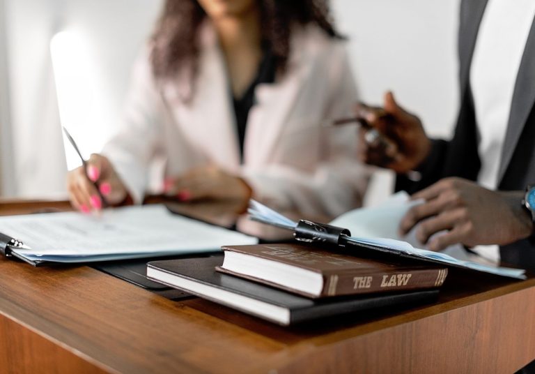 Duas pessoas analisam documentos e livros de direito em uma mesa. Curso: Noções Básicas de Direito Cooperativo.
