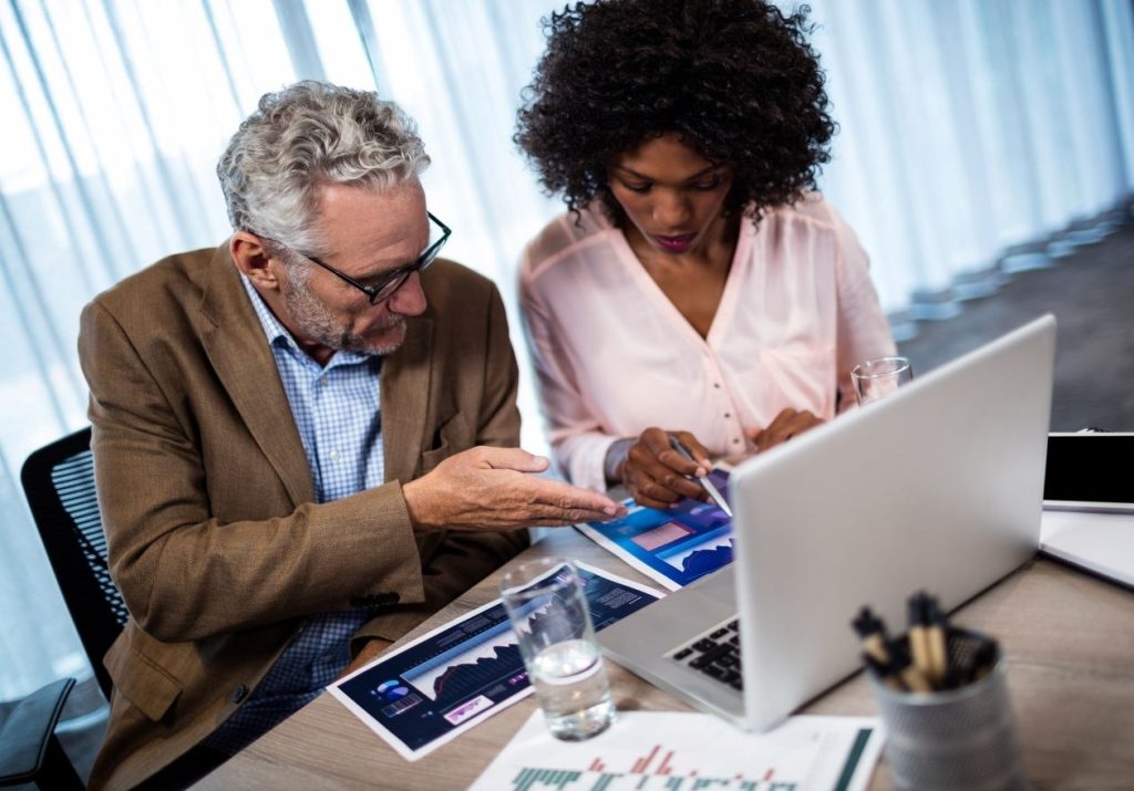 Homem e mulher analisam dados em laptop sobre a mesa de um escritório. Curso: Gestão Econômica e Financeira de Cooperativas.
