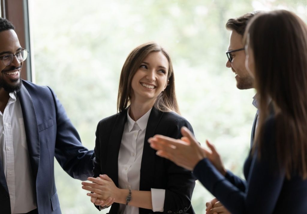 Pessoas conversam e sorriem em ambiente profissional com ampla janela ao fundo. Curso: Integração do Novo Colaborador Unimed.