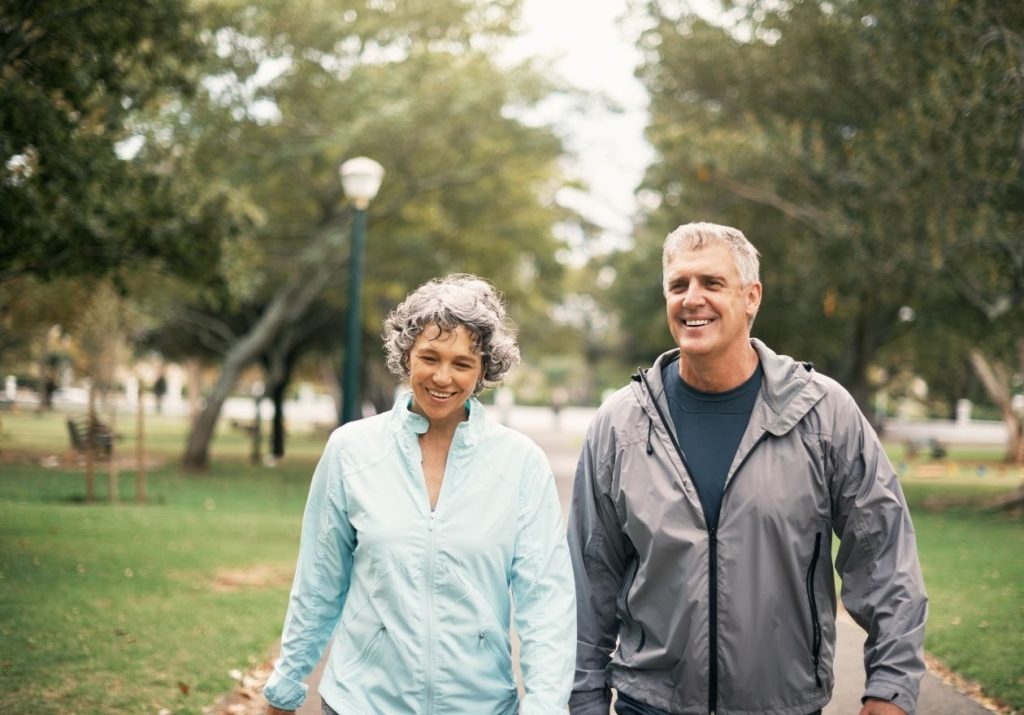 Casal caminha de mãos dadas em um parque arborizado, sorrindo e aproveitando o dia. Curso: Melhorar a Qualidade de Vida.